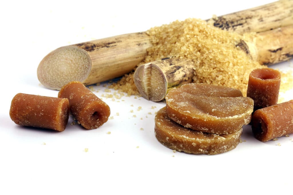 Sugar cane pieces, unrefined brown sugar, and granulated brown sugar on a white background.