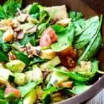 Fresh spinach salad with avocado, bacon, and diced tomatoes in a wooden bowl.