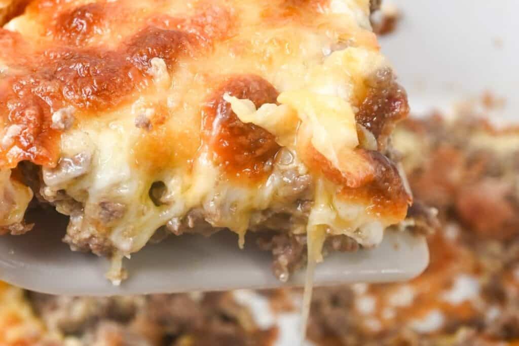 A close-up of a slice of lasagna being lifted, showing melted cheese and layered meat and sauce.