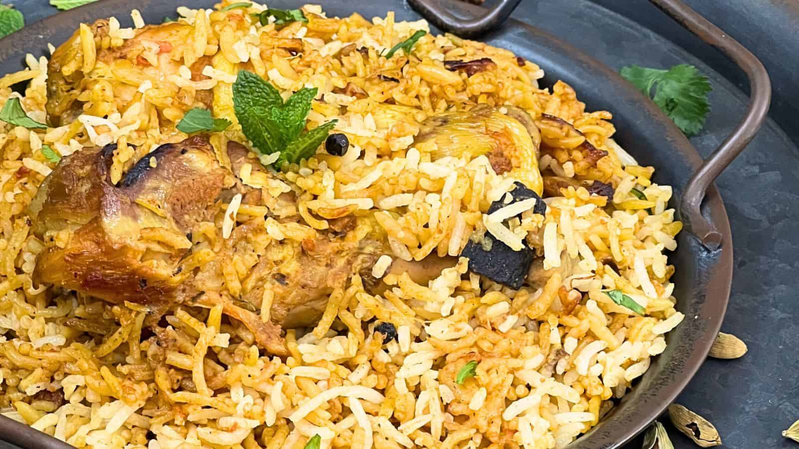 Close-up image of chicken biryani in a copper dish, garnished with mint and coriander leaves.