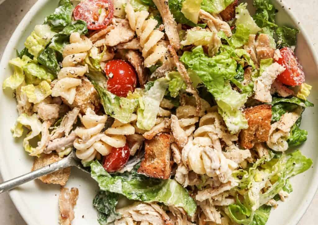 A plate of caesar salad with chicken, croutons, cherry tomatoes, and a creamy dressing, with a fork.