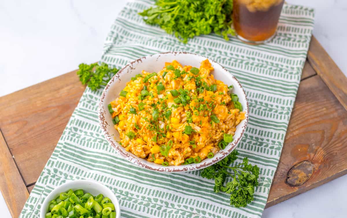 A bowl of rice with corn and herbs on a striped cloth with garnishes on the side.