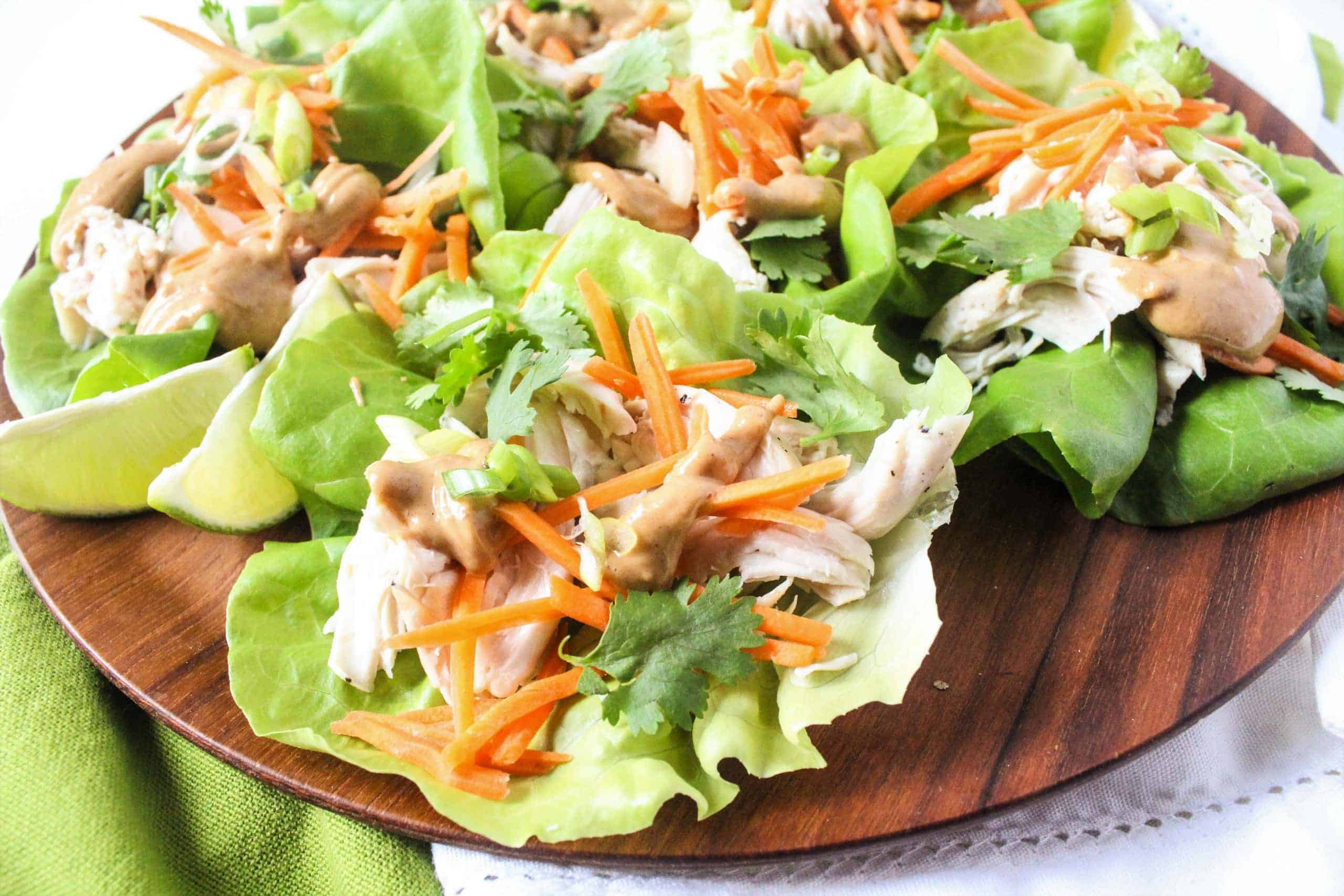 Lettuce wraps filled with shredded chicken, shredded carrots, and peanut sauce on a plate.