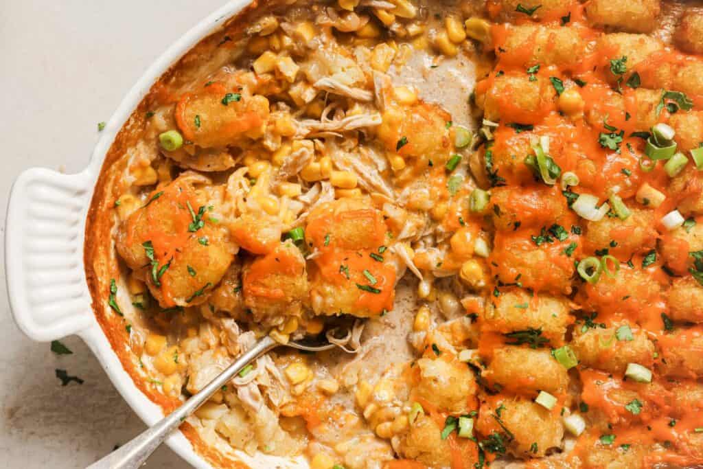 Overhead view of a chicken tater tot casserole in a white dish, topped with sliced green onions and parsley.