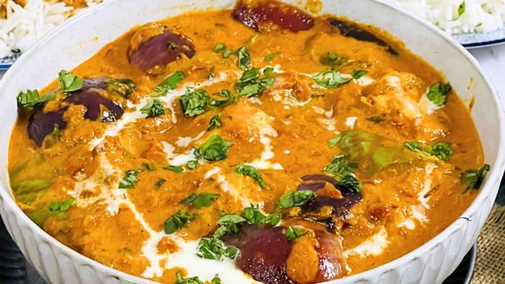 A bowl of creamy chicken tikka masala garnished with fresh herbs, served alongside a dish of rice.