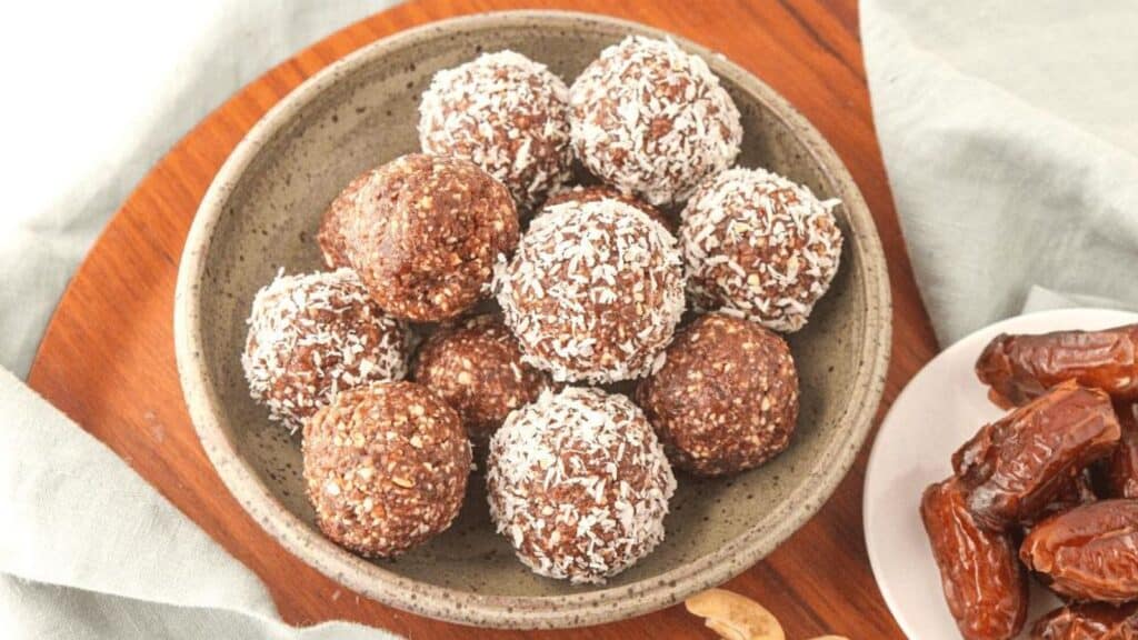 A bowl of Chocolate Cashew Bliss Balls is placed on a wooden serving board.