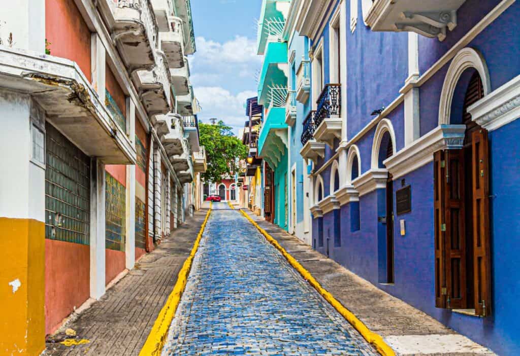 Narrow cobblestone street lined with vibrant, colorful colonial buildings under a bright blue sky.