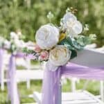 Outdoor wedding chairs decorated with purple ribbons and floral arrangements at an outdoor setting.