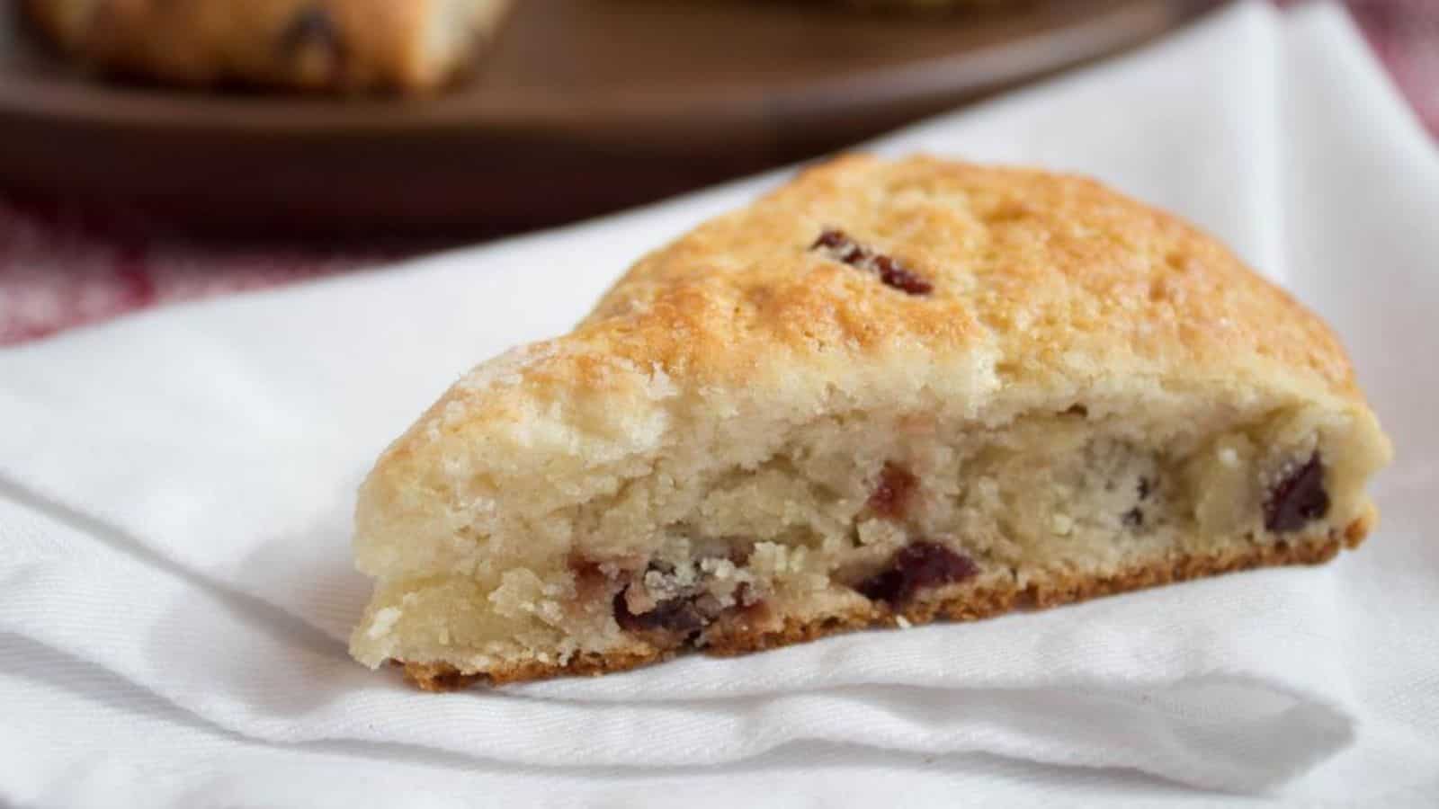 A triangular cranberry scone sitting on a white linen napkin.