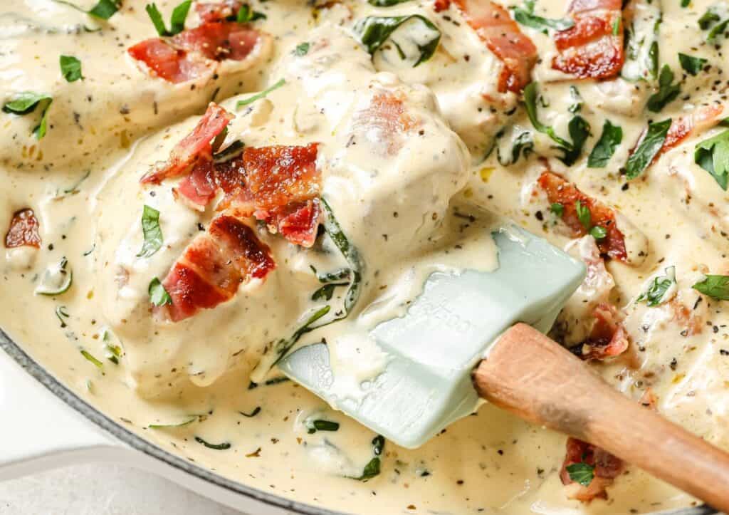 Creamy chicken dish garnished with bacon and herbs in a skillet.
