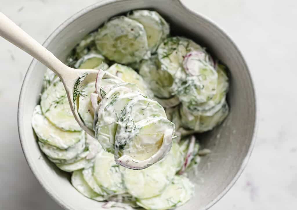 Creamy cucumber salad with dill in a bowl with a serving spoon.