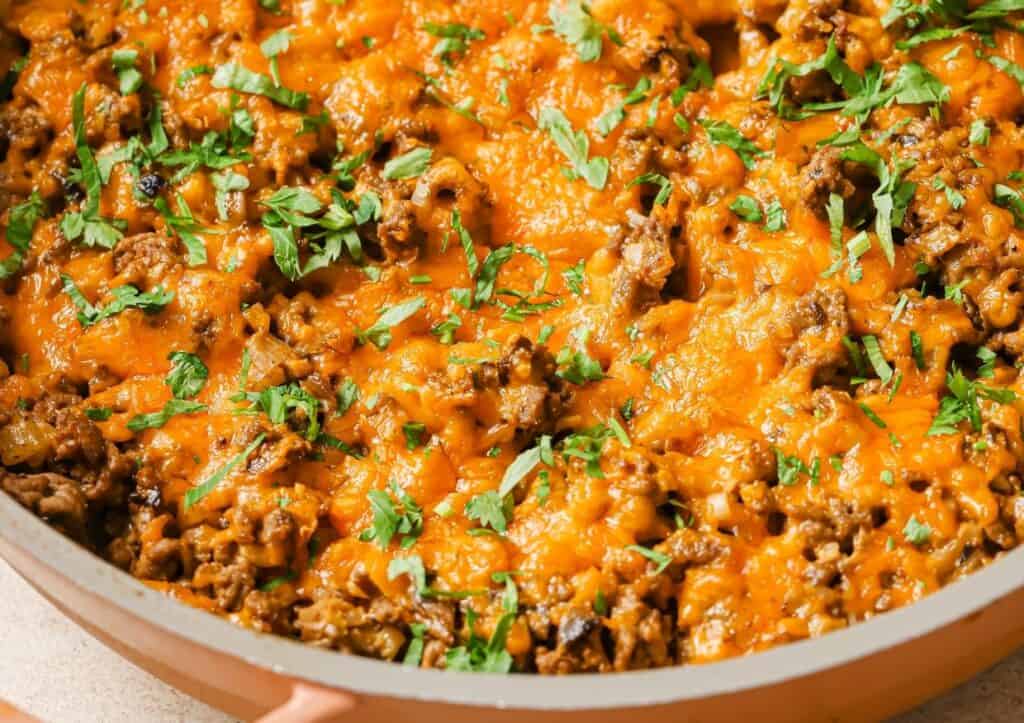 Ground meat dish topped with melted cheese and garnished with herbs in a skillet.
