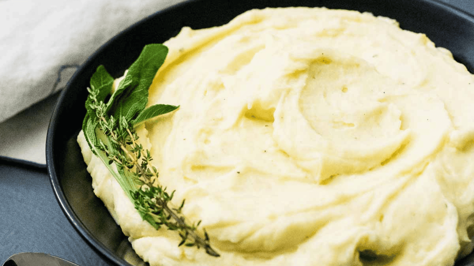 A bowl of mashed potatoes with gravy and sprigs of thyme and sage.