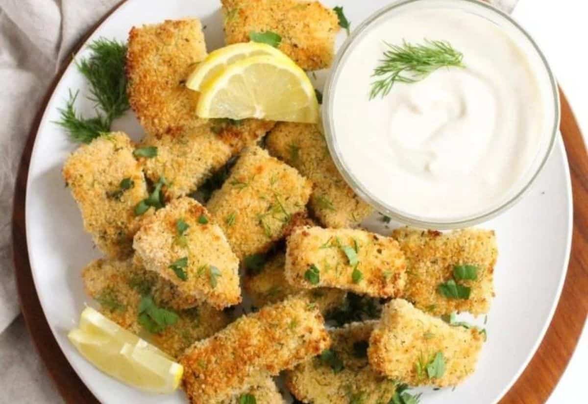 A white plate with salmon bites next to small bowl of creamy honey mustard yogurt dipping sauce.