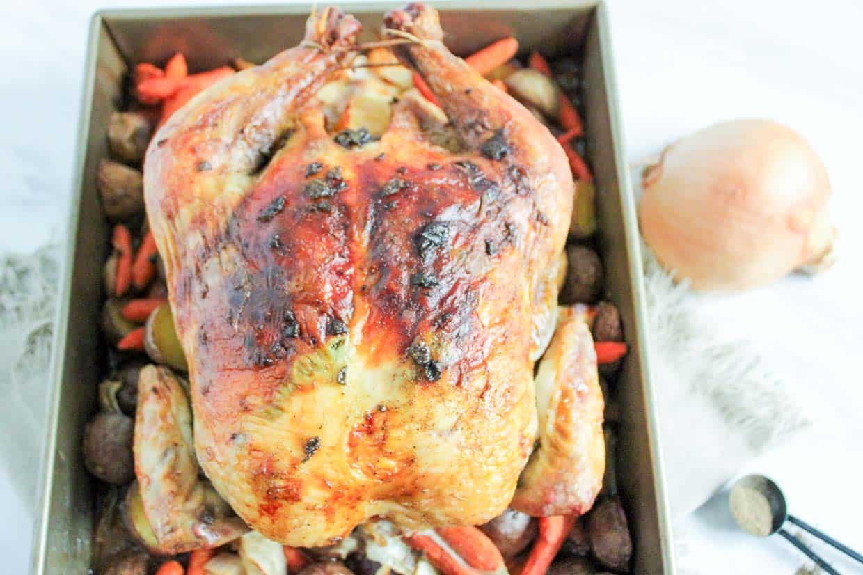 Roasted chicken nestled amongst potatoes, onions, and carrots in the baking pan.