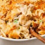 A creamy tuna noodle casserole with peas and a crispy breadcrumb topping in a white dish with a wooden spoon.