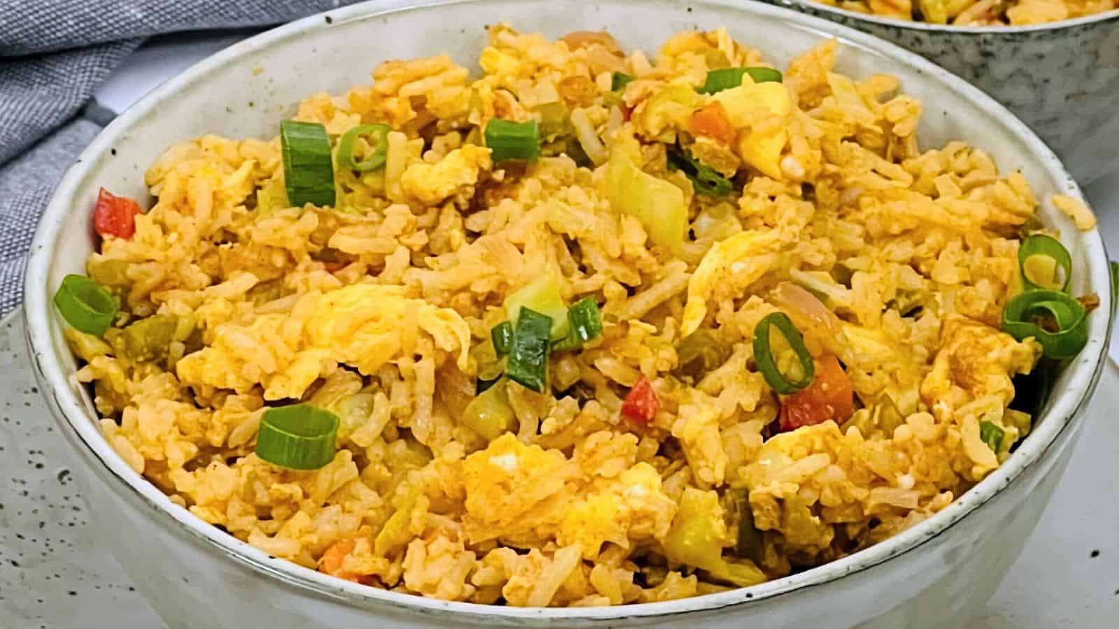 A bowl of Egg Fried Rice with green onions, and diced vegetables, served in a speckled ceramic bowl.