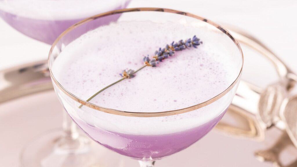 A lavender cocktail garnished with a sprig of lavender, served in an elegant glass.
