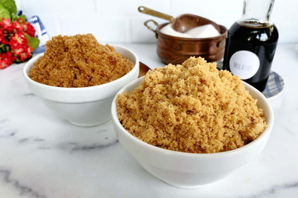 Two bowls of brown sugar with a bottle of molasses in the background.