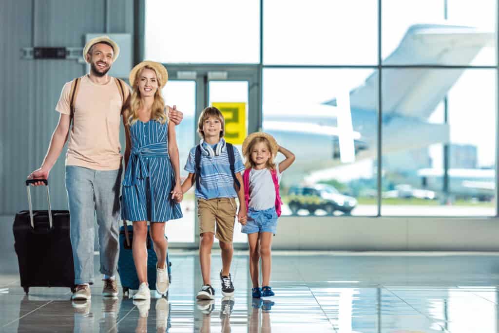 A family of four walking happily through an airport terminal with their luggage.