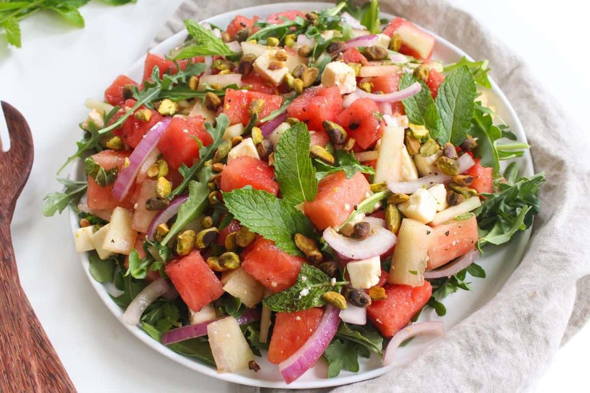 A plate with watermelon chunks, feta cheese, arugula, pistachios, and red onion mixed together.