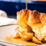 Maple syrup pouring over a stack of golden-brown french toast on a plate.