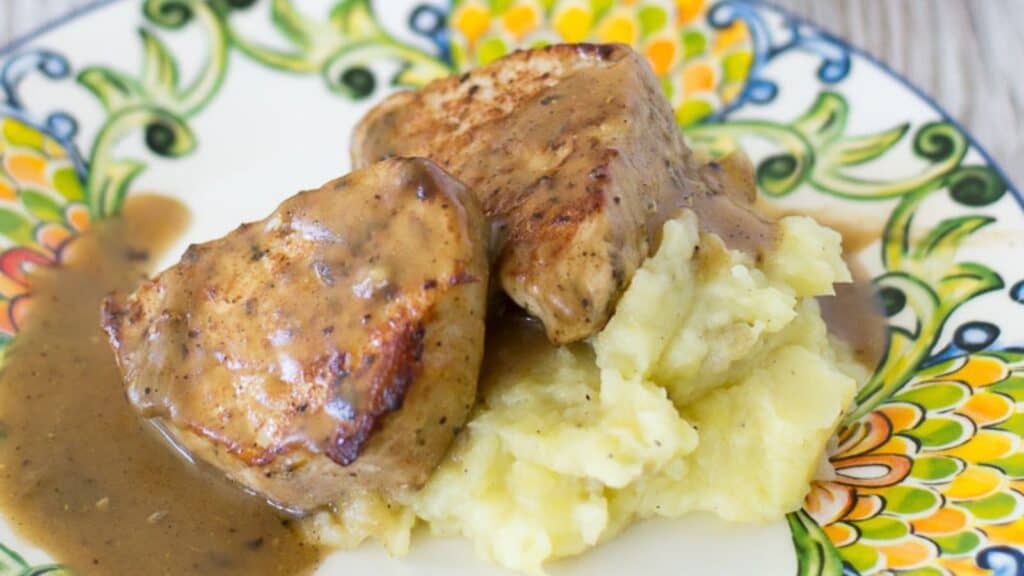Pork chops in gravy served with mashed potatoes on a decorative plate.