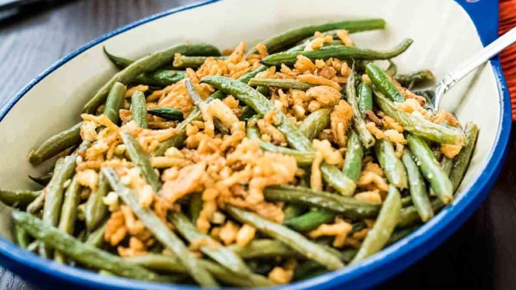 A dish of green beans and crumbled tempeh served in a blue-rimmed white bowl.