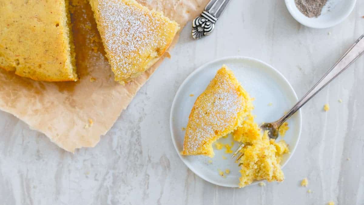 Orange glazed cardamom cake on a white plate with a fork.