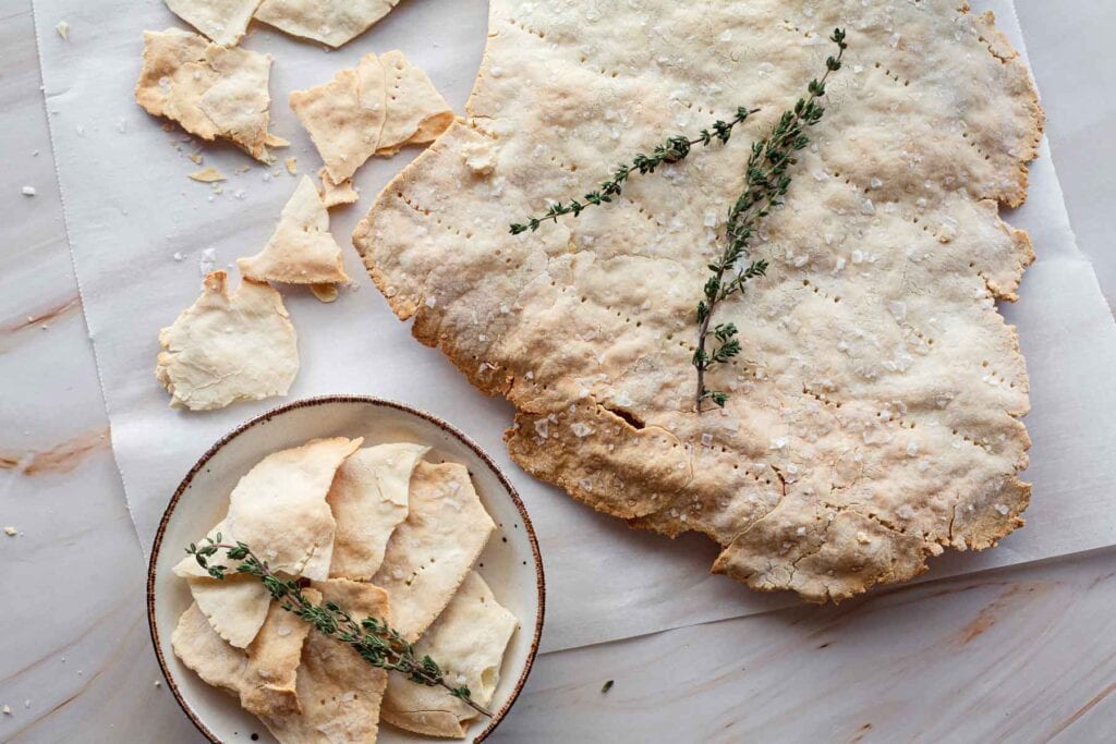 Homemade flatbread with fresh thyme on a marble surface, some pieces are whole and others are broken into smaller chunks placed on a small plate.