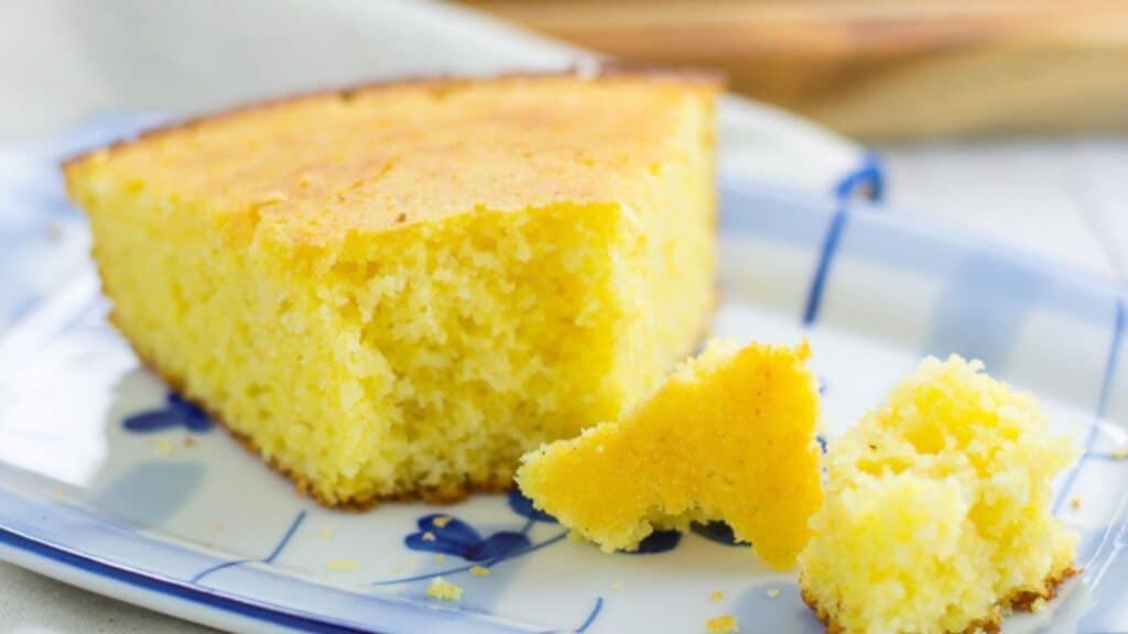 A slice of cornbread on a plate with a small piece broken off.