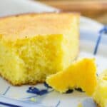 A slice of cornbread on a plate with a small piece broken off.