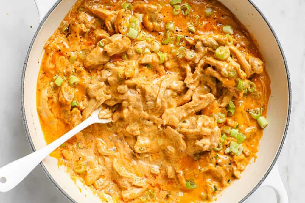 Green chile chicken in a white pot, garnished with sliced green onions, served with a spoon.