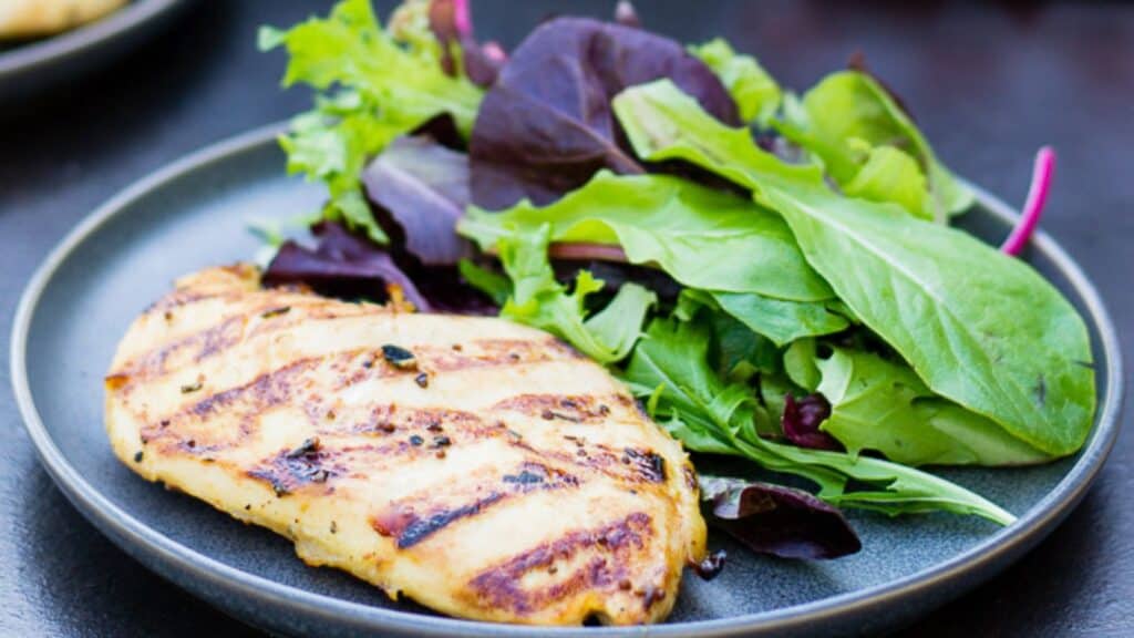 Grilled chicken breast served with a side of mixed greens on a plate.