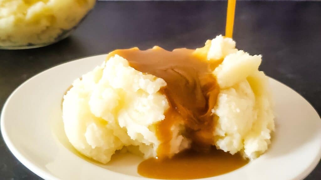 Mashed potatoes with gravy being poured on top.