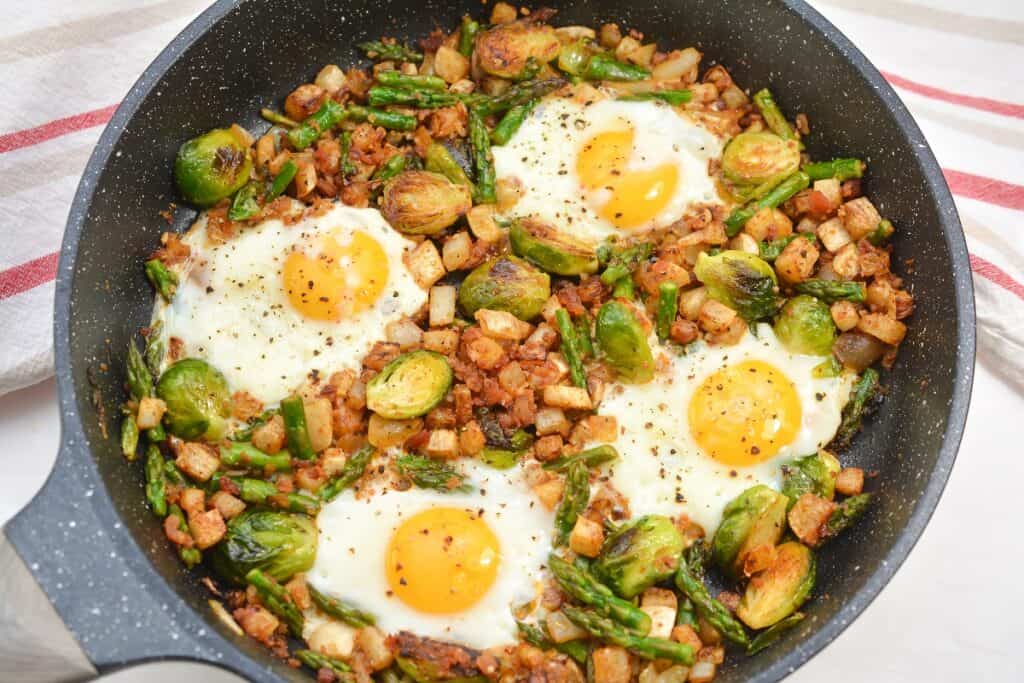 A skillet containing a meal with brussels sprouts, eggs, and diced potatoes.