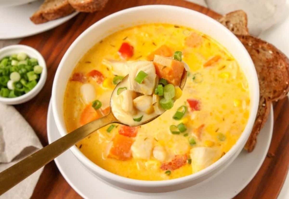 A bowl of seafood chowder with a spoon being held above it.