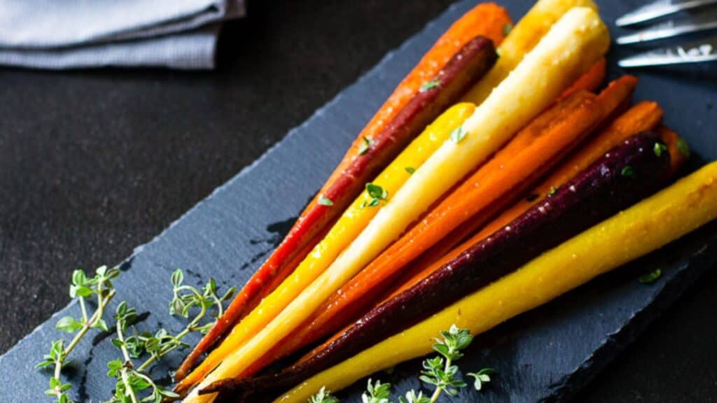 Colorful roasted carrots arranged on a slate serving platter, garnished with fresh herbs.