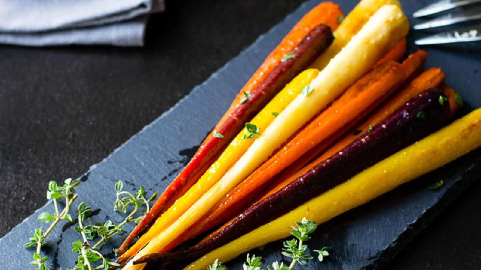 Red, yellow, and orange honey glazed carrots on a slate board.