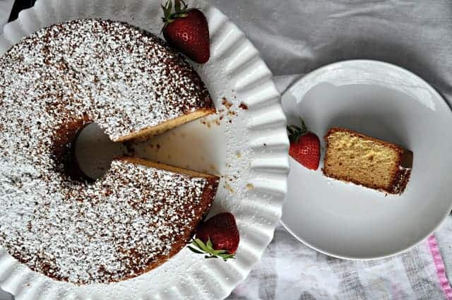 A bundt cake with powdered sugar on top, served with strawberries and a single slice placed on a separate plate.