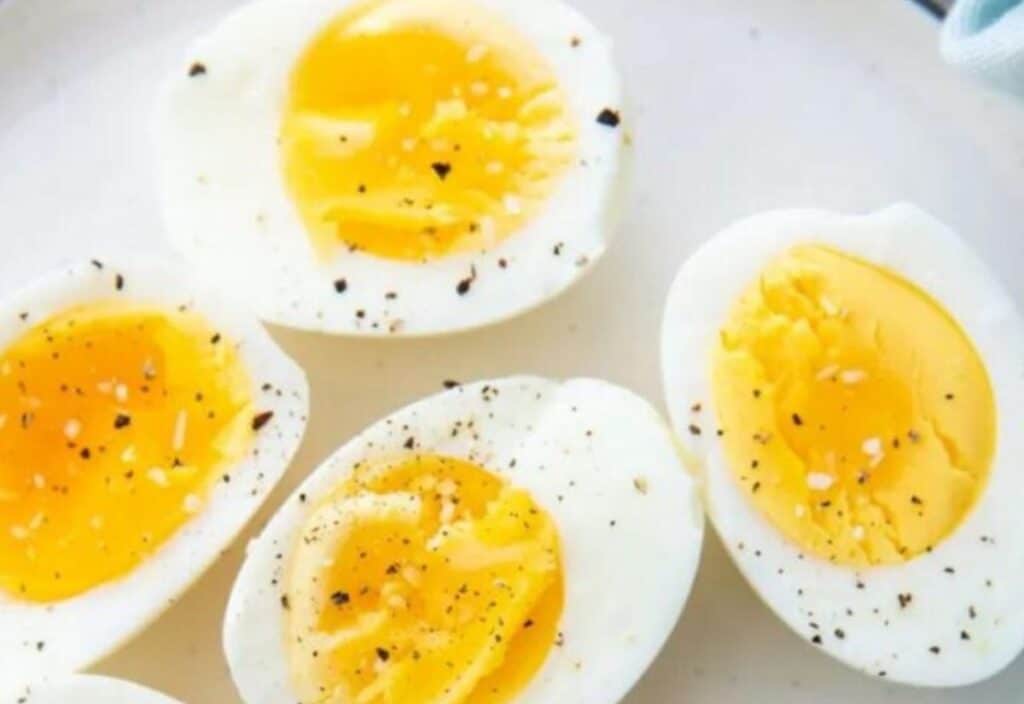 Halved hard-boiled eggs on a plate, sprinkled with black pepper. two eggs are soft-boiled with runny yolks, and two are fully cooked.