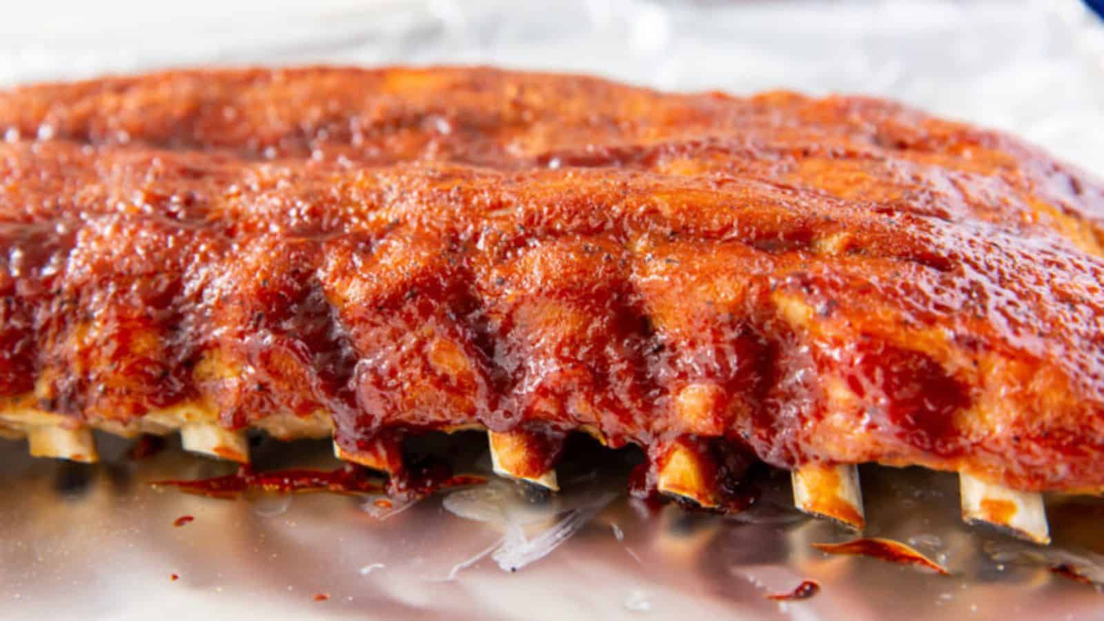 Instant Pot Baby Back Rib dipped in barbeque sauce in a glass bowl