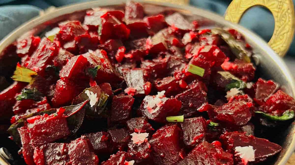 A bowl of diced Beetroot Palya garnished with herbs and sprinkled with salt, served on a dark textured background.