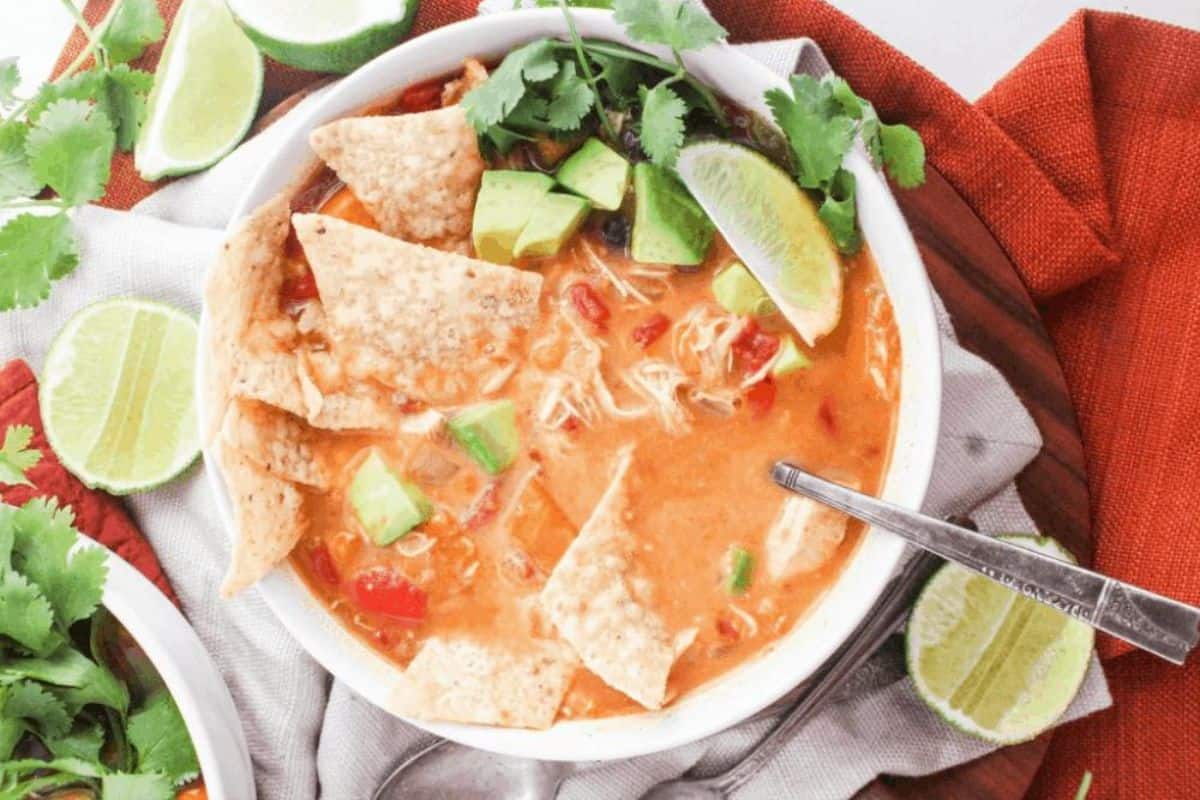 A bowl of chicken tortilla soup with tortilla chips, diced avocado, and sliced lime on top.