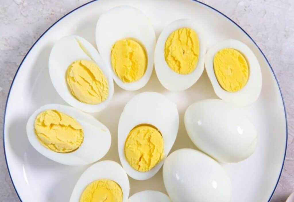 A white plate holding several hard-boiled eggs, some cut in half to show the yellow yolk, on a light surface.
