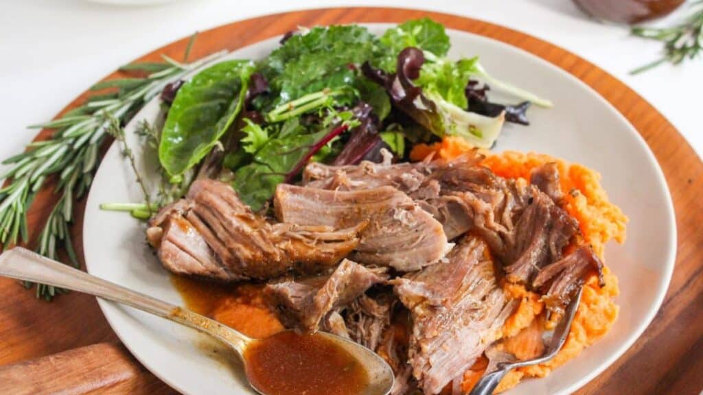 A plate of pulled pork with mashed sweet potatoes and a side of mixed greens salad.