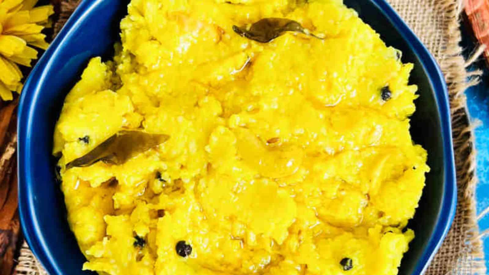 A bowl of Ven Pongal with curry leaves, served on a colorful woven mat.