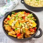 Kung Pao Chicken in a bowl with a bowl of rice in the background.