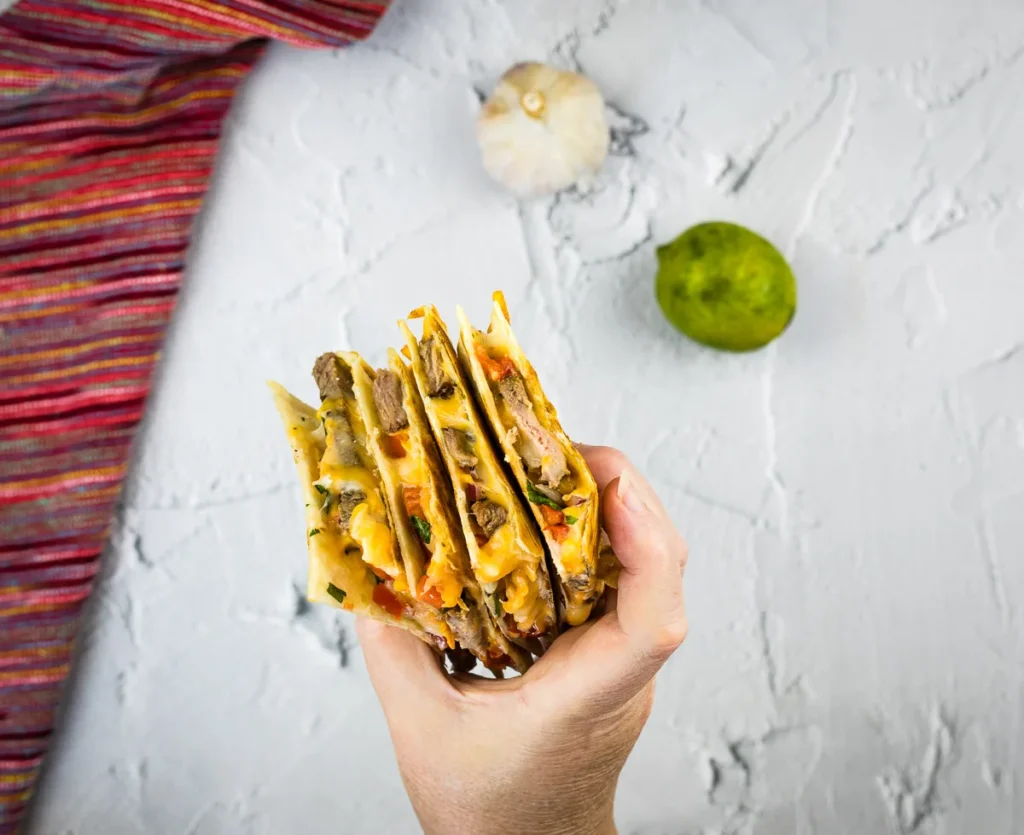 A hand holding a cut steak quesadilla.