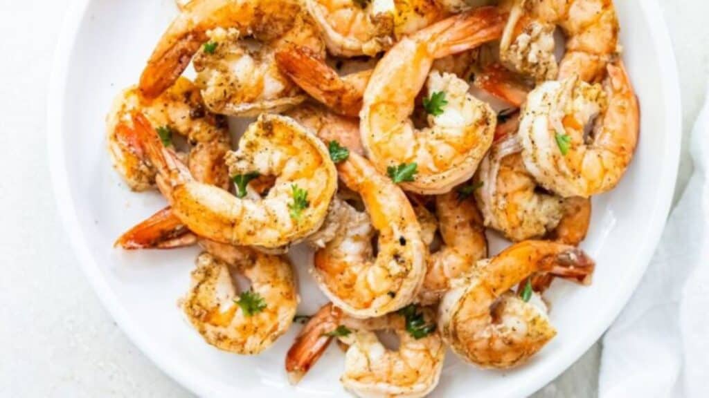 A plate of seasoned grilled shrimps garnished with parsley on a white background.